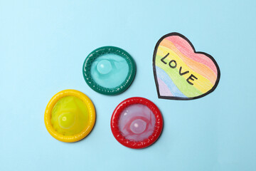 Multicolored condoms and heart in LGBT colors with text Love on blue background