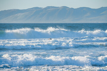 Stormy Pacific ocean and one flying bird, mountains and clear blue sky on background, CA