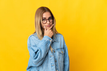 Young blonde woman isolated on yellow background having doubts
