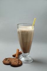 Glass of chocolate milkshake, cookies and cinnamon on gray background