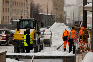 Workers with shovels and special equipment remove snow from the streets of the city after a snowfall. Snowfall in Moscow. Soft focus.