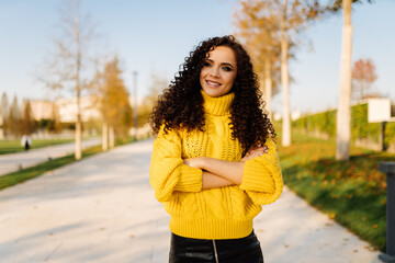 Folding on her chest the hands of a girl in a bright yellow sweater cute smiling stands on the park track. High quality photo