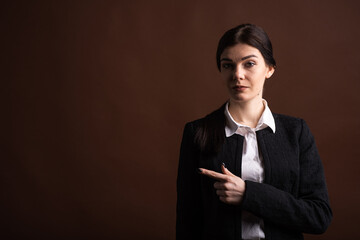 Portrait of serious brunette business woman pointing her finger to the side in studio on brown...