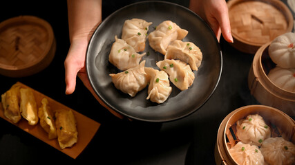 Female hands holding a plate of dumplings to serve on Dimsum table in Chinese restaurant
