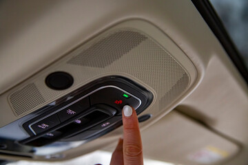 female driver's finger presses the sos button on the ceiling panel of a modern car