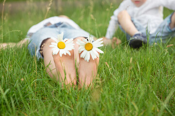 Boy lying on green grass outdoors in park. Happy summer feet. Child with daisy lying in sunny...