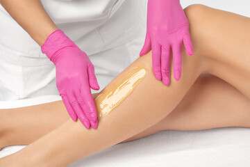 A beautician makes a sugar paste depilation of a woman's legs in a beauty salon. Female aesthetic...