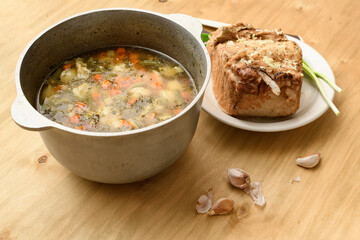 cauldron of soup and baked meat on a plate, green onion and garlic on wooden background, home cooking