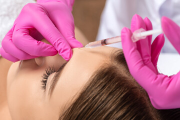 Cosmetologist makes rejuvenating anti wrinkle injections on the face of a beautiful woman. Female...