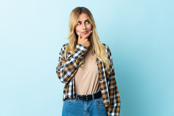 Young blonde Uruguayan isolated on blue background having doubts and with confuse face expression