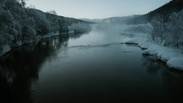 Time lapse video of a beautiful mountain river in winter. A mist is formatting and  changing over the river . Trees on the banks of the river are  covered in ice
