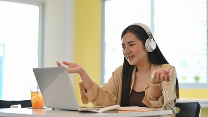 Female student with headphone talking while study online on laptop in living room