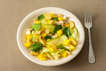 Plate with salad and fork close-up on a brown background, salad of cucumber and chicken breast, mozzarella and croutons with sweet mango pieces and spinach