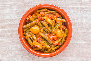 Green bean dish with ham, potato and tomato sauce on a clay plate on a wooden table. Top view.