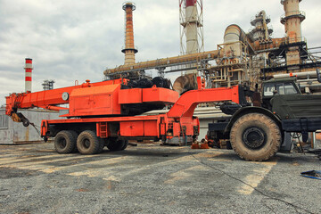 A heavy-duty truck crane with a folded boom stands on the industrial site of an oil refinery