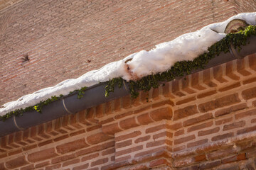 Detail of a gutter with snow on a brick wall on a cold winter's day.