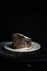 Chocolate pie on a white plate with a sugar powder on top on the black background.