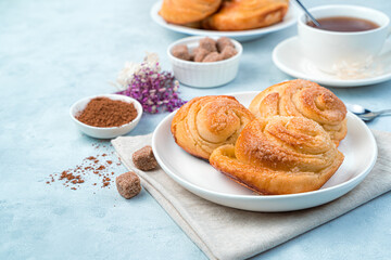Fresh rolls on a plate, cocoa, sugar and tea on a blue background.