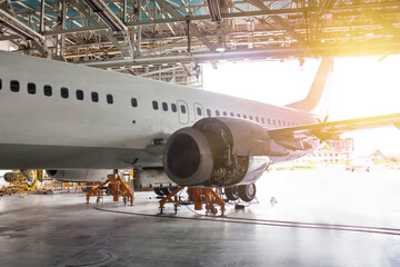 White passenger airliner under maintenance in the hangar. Repair of jet plane engine on the wing and checking mechanical systems for flight operations