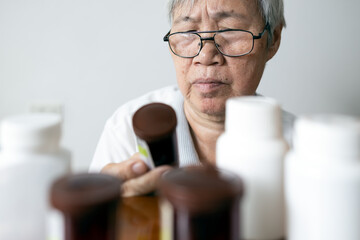 Asian senior woman holding drug bottle in front of medicine cabinet in her home,reading the label...