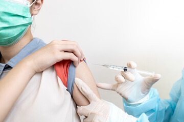 Female doctor with syringe doing injection vaccine COVID-19, flu in the shoulder or arm of lady...
