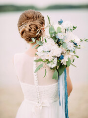 Wedding day. Bride in a wedding dress holds tender bridal bouquet with white and blue flowers near the sea beach
