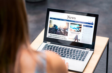 News website in laptop screen with online article and headline. Woman reading newspaper or magazine...