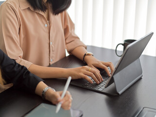 Male hands typing on tablet keyboard while sitting next to co worker in meeting room