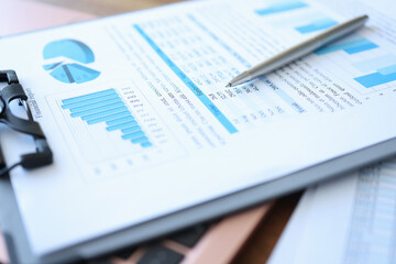 Clipboard with financial report and pen lie on table