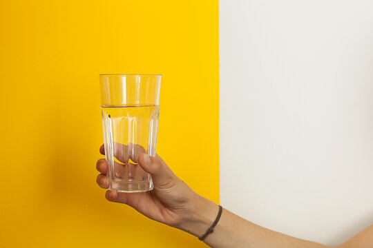  glass of clean drinking water in beautiful female hands. bright yellow background.