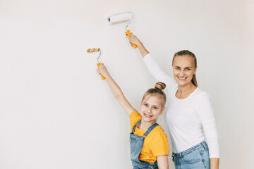Beautiful and happy mom and daughter paint the walls in the apartment white