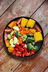 Mixed vegetables in the round baking pan are waiting for the baking on the wooden table, rustic style, super healthy, close-up, top view