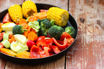 Mixed vegetables in the round baking pan are waiting for the baking on the wooden table, rustic style, super healthy, close-up, top view