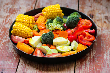Mixed vegetables in the round baking pan are waiting for the baking on the wooden table, rustic style, super healthy, close-up, top view