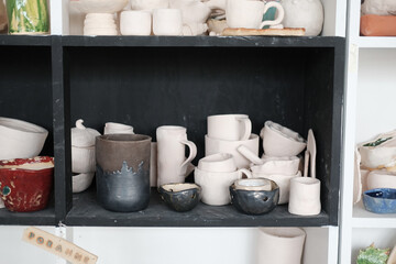 Clay products of different sizes. Colorful kitchen items on the shelf. Handmade plates and cups