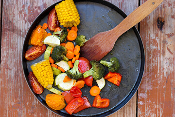 Super tasty oven roasted vegetables in black baking dish are lying on the wooden table, super...
