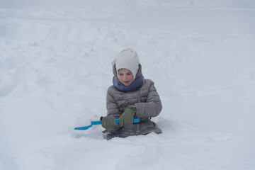 Fototapeta na wymiar The girl is digging the snow. The child plays with a lot of snow. A rosy child in the cold. Nice walk and play