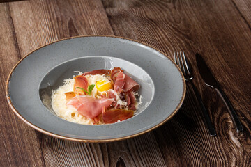 Pasta Carbonara. Spaghetti with bacon, parmesan, cream sauce and egg yolk. Isolated dish on a grey round plate with silver cutlery on wooden background. Mediterranean gourmet food.