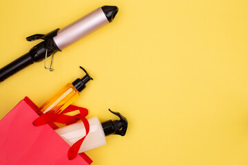Hairdressing tools in black: curling tongs, hair brush, spray in red gift bag on yellow background,...