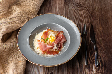 Pasta Carbonara. Spaghetti with bacon, parmesan, cream sauce and egg yolk. Isolated on a grey round plate with silver cutlery and sacking on wooden background. Mediterranean gourmet food.