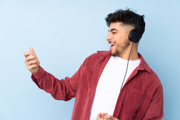 Arabian handsome man isolated on blue background listening music and doing guitar gesture