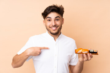 Arabian man eating sushi isolated on beige background with surprise facial expression