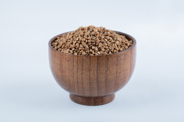 A small wooden bowl full of buckwheat on white background