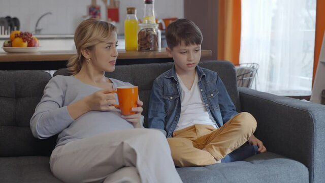 Pregnancy, maternity concept.Pregnant mother talking with her little son while drinking coffee or tea.