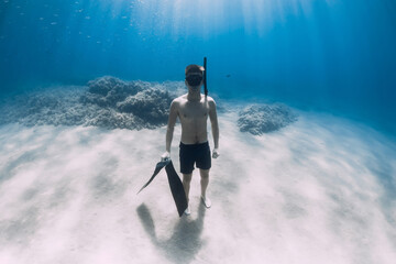 Sporty man freediver stay with fins on sandy bottom underwater in blue sea.