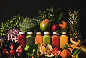 Variety of fresh smoothies or juices for detox weight loss diet. Colorful juices in bottles with fruit, vegetables and greens around, dark background. Vegan, vegetarian, clean eating, alkaline food