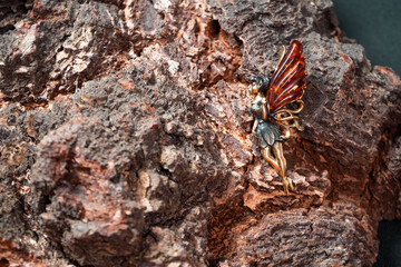 Suspension in the form of a fairy with wings of brass and amber against the background of a tree