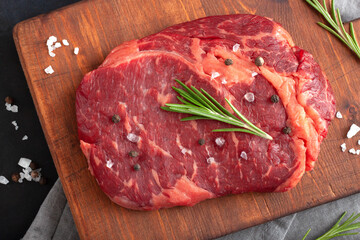 Raw rib eye steak of beef with rosemary on cutting board