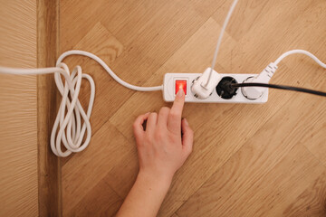 Top view of female hand turn on the extension cord at home. White cable connector