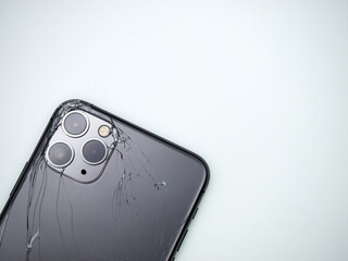 The back of the space grey modern smartphone has broken glass on white background. Modern smartphone with damaged back glass.